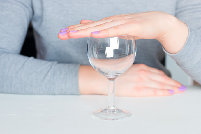 Mujer tapando una copa con la mano como símbolo de los beneficios de no beber alcohol.